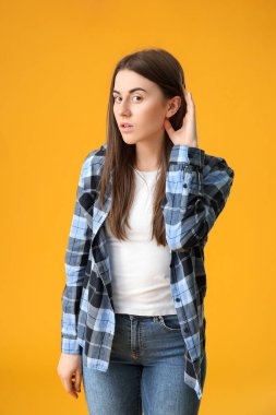 Genç bir kadın renkli arka planda bir şeyler duymaya çalışıyor.