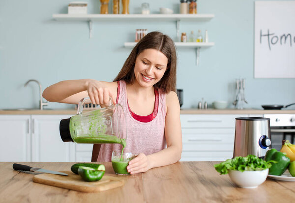 Sporty woman pouring healthy smoothie into glass in kitchen