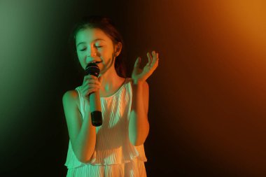 Sevimli küçük kız karanlık arka planda şarkı söylüyor.