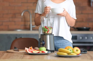 Genç bir kadın mutfakta smoothie yapıyor.