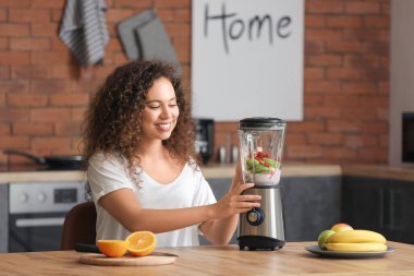 Genç bir kadın mutfakta smoothie yapıyor.