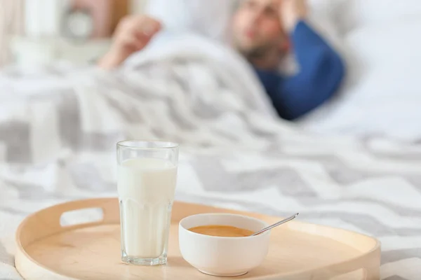 带有健康牛奶和蜂蜜的托盘放在患感冒的人的床上 — 图库照片