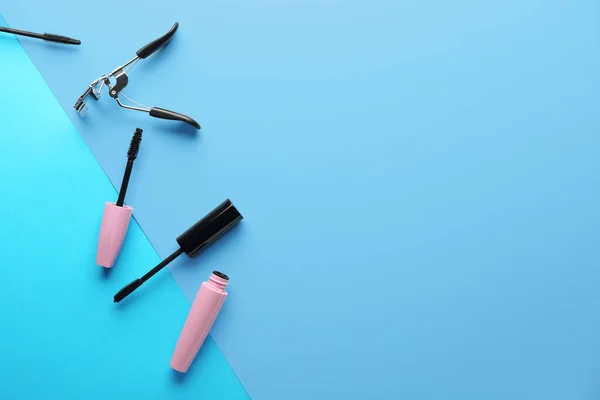 Mascara and eyelash curler on color background