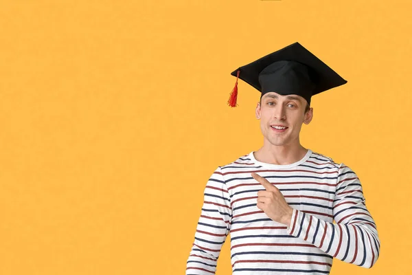 卒業帽子の若者が何かを指差す色の背景 — ストック写真