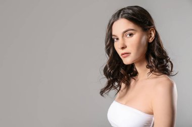 Gri arkaplanda kısa dalgalı güzel saçları olan genç bir kadın.