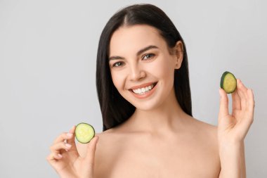 Salatalık dilimleri ve açık arkaplanda güzel genç bir kadın.