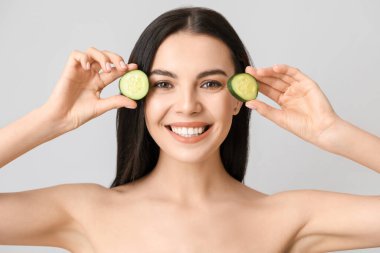 Salatalık dilimleri ve açık arkaplanda güzel genç bir kadın.