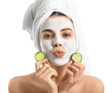 Beyaz arka planda salatalık dilimleri ve yüz maskesi olan güzel genç bir kadın.