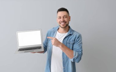 Gri arka planda dizüstü bilgisayarı olan yakışıklı bir adam.