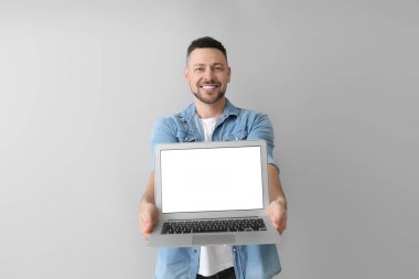 Gri arka planda dizüstü bilgisayarı olan yakışıklı bir adam.