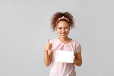 Tablet bilgisayarlı güzel bir Afro-Amerikalı kadın gri arka planda baş parmağını kaldırıyor.