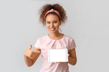 Gri arka planda tablet bilgisayarı olan güzel bir Afro-Amerikalı kadın.