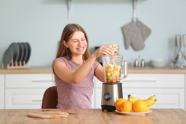 Genç bir kadın mutfakta smoothie yapıyor.