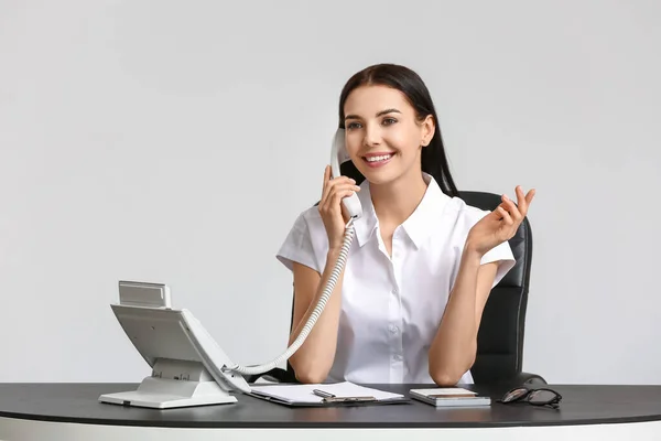 Beautiful young secretary talking by telephone at table on white background