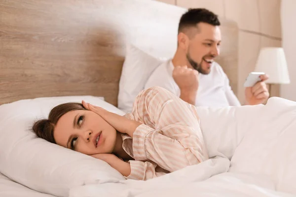 Young woman cannot sleep because of her husband playing game on mobile phone in bedroom