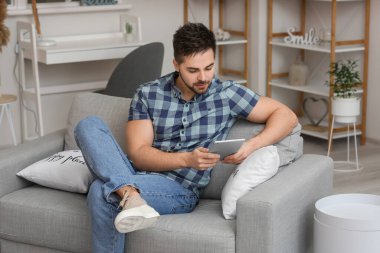 Evde tablet bilgisayarı olan genç bir adam.