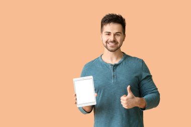 Tablet bilgisayarlı genç adam renk arkaplanında başparmak yukarı gösteriyor