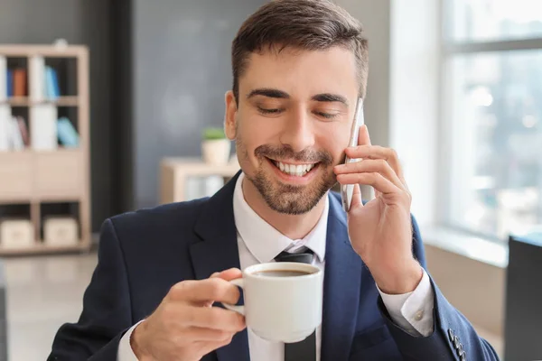 Genç Işadamı Elinde Bir Fincan Sıcak Kahveyle Ofiste Telefonla Konuşuyor — Stok fotoğraf