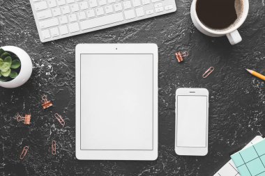 Tablet bilgisayar, cep telefonu, PC klavye, koyu arkaplanda bir fincan kahve ve kırtasiye.