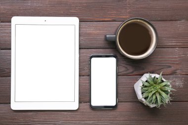 Tablet bilgisayar, cep telefonu ve tahta arka planda bir fincan kahve.