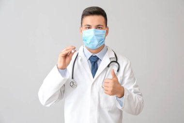 El feneri olan erkek doktor gri arka planda baş parmak işareti gösteriyor.
