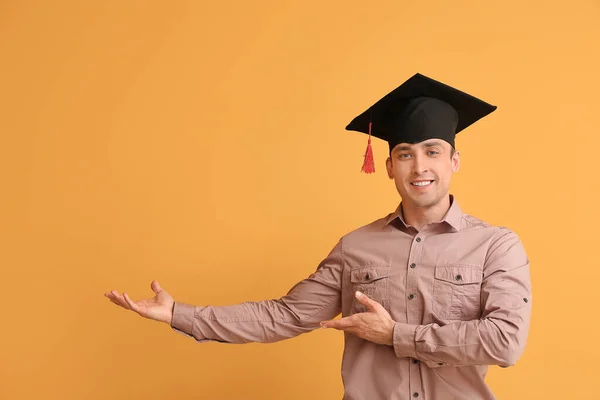 卒業帽子の若者が色の背景に何かを示しています — ストック写真