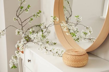 Çiçek açan ağaç dalları ve odadaki çekmecelerin üzerinde sepet olan ayna.