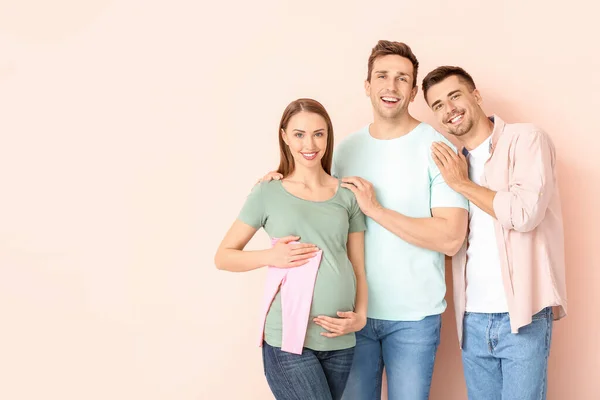 Schwules Paar Und Schwangere Frau Mit Babykleidung Auf Farbigem Hintergrund — Stockfoto