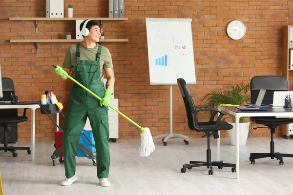 男性の清掃員は音楽を聴きながらオフィスの床を掃除する — ストック写真