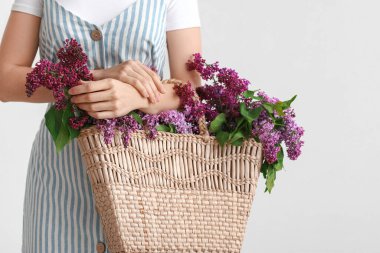 Beyaz arka planda çanta ve leylak çiçekleri olan güzel genç bir kadın.