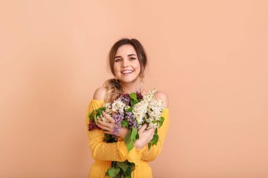 Beautiful young woman with lilac flowers on color background