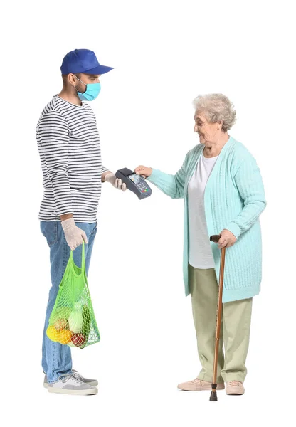 Elderly woman paying courier of food delivery company for order via terminal against white background