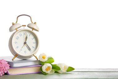 Alarm saati, kitaplar ve çiçekler beyaz arka planda. Bahar geldi.