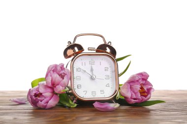 Çalar saat ve çiçekler beyaz arka planda. Bahar geldi.