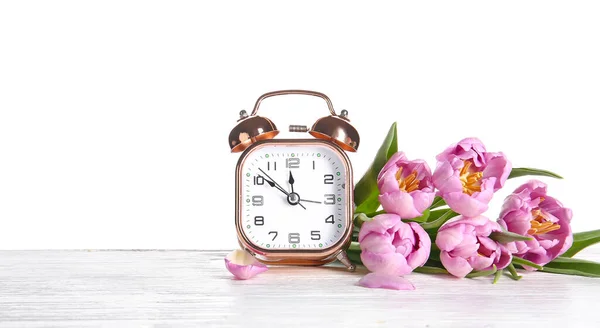 白い背景に対してテーブルの上の目覚まし時計と花 春の時間 — ストック写真