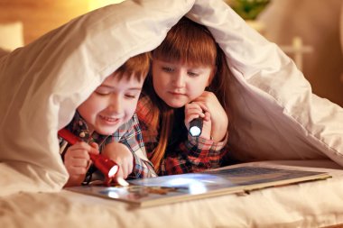 Geceleri battaniyenin altında kitap okuyan küçük çocuklar.