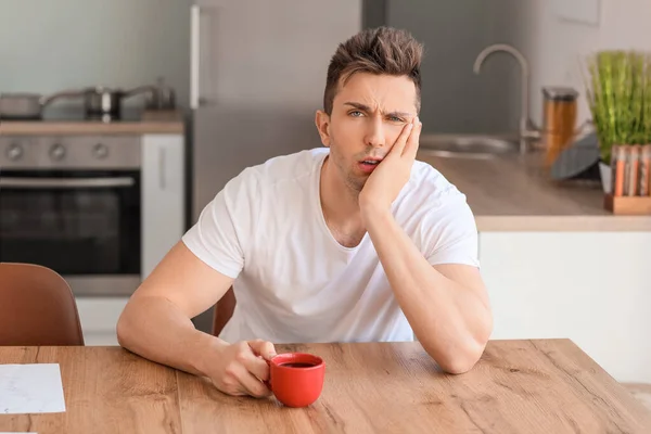 Sleepy man drinking coffee in kitchen