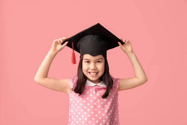 Little girl in graduation hat on color background