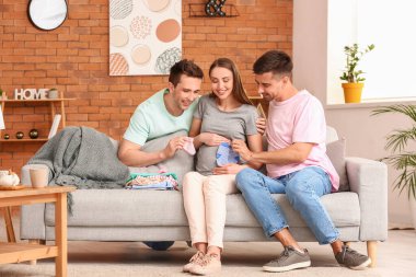 Gay couple and pregnant woman with baby clothes at home clipart
