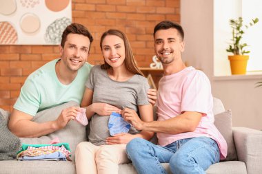 Gay couple and pregnant woman with baby clothes at home clipart