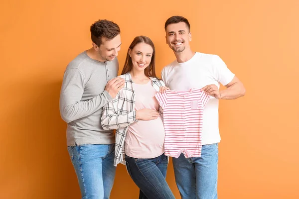 Schwules Paar Und Schwangere Frau Mit Babykleidung Auf Farbigem Hintergrund — Stockfoto