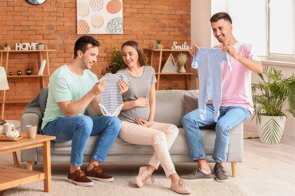 Гей пара и беременная женщина с детской одеждой дома
