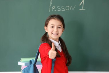 Sınıfta tahtada baş parmağını kaldıran sevimli küçük bir öğrenci.