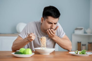 Young man with anorexia eating noodles at home clipart