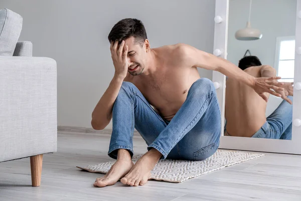 Displeased man with anorexia near mirror at home