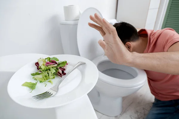 厕所附近患厌食症的年轻人和浴室里有沙拉的盘子 — 图库照片