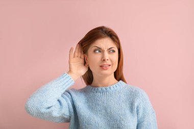 Genç bir kadın renkli arka planda bir şeyler duymaya çalışıyor.