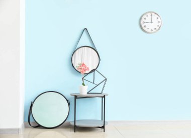 Oturma odasındaki renkli duvarın yanında bitki ve aynalar olan masa.