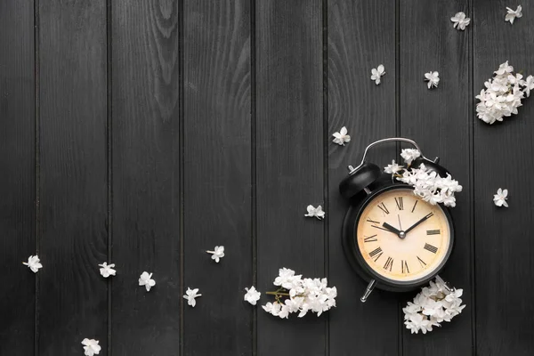 Alarm clock and flowers on dark wooden background. Spring time