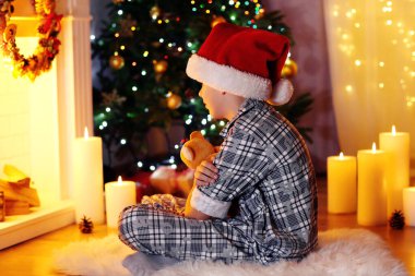 Küçük çocuk şöminenin yanında oturuyor.